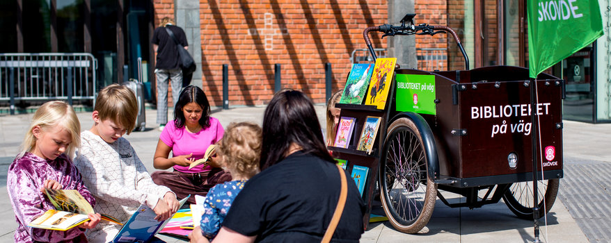 En man och två kvinnor som står vid en bokcykel fylld med böcker. På cykeln står det "Biblioteket på väg"